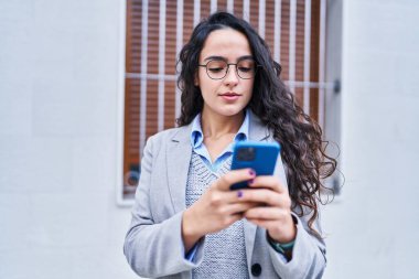 Genç İspanyol kadın yönetici caddede akıllı telefon kullanıyor.