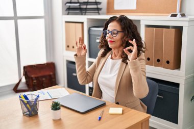 Middle age hispanic woman working with laptop doing yoga pose at the office
