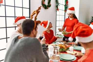 Bir grup genç, mutlu bir şekilde gülümseyerek evde Noel yemeği yiyor..