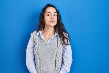 Young brunette woman standing over blue background looking at the camera blowing a kiss on air being lovely and sexy. love expression. 