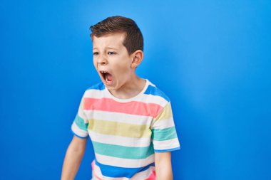 Kafkasyalı genç, mavi arka planda öfkeli ve kızgın bir şekilde bağırıyor öfkeyle bağırıyor. öfke ve agresif konsept. 