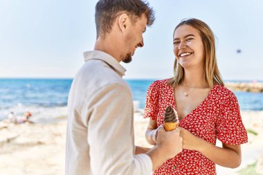 Genç İspanyol çift tatilde gülümseyerek kumsalda dondurma yiyor.