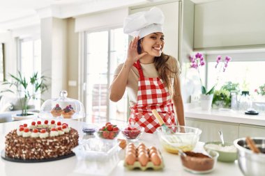 Güzel, genç, esmer, pasta şefi kadın mutfakta pasta pişirirken kulağına fısıldayarak dedikoduları ve dedikoduları dinliyor. Sağırlık kavramı. 