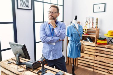 Orta yaşlı bir adam perakende mağazasında yönetici olarak çalışıyor. Elleri çenesinde soru sormayı düşünüyor. Düşünceli bir ifade. Düşünceli bir yüzle gülümsüyor. şüphe kavramı. 