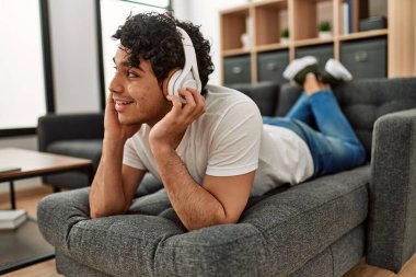 Genç İspanyol adam evdeki kanepede müzik dinliyor..