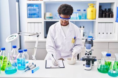 Bilim adamı üniforması giyen Afrikalı Amerikalı bir kadın laboratuarda çalışan bir panoya yazı yazıyor.