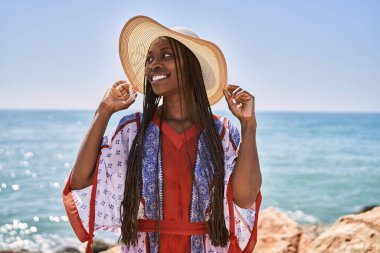 Sahilde duran, yaz şapkası takan genç Afrikalı Amerikalı kadın..