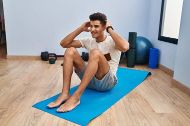 Genç İspanyol adam gülümsüyor spor merkezinde kendine güvenen karın kasları egzersizi yapıyor.