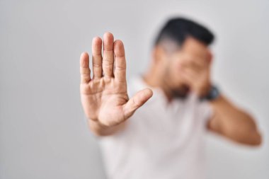 Sakallı, beyaz arka plan üzerine günlük kıyafetler giyen, elleriyle gözlerini kapatan, üzgün ve korku ifadeli hareketlerini durduran genç İspanyol bir adam. utangaç ve olumsuz kavram. 