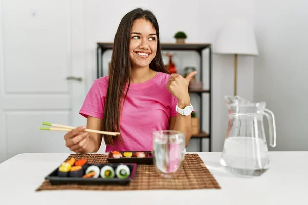 若いですブルネット女性食べる寿司箸を笑顔で幸せな顔を見ながらと親指アップで側面を指す — ストック写真