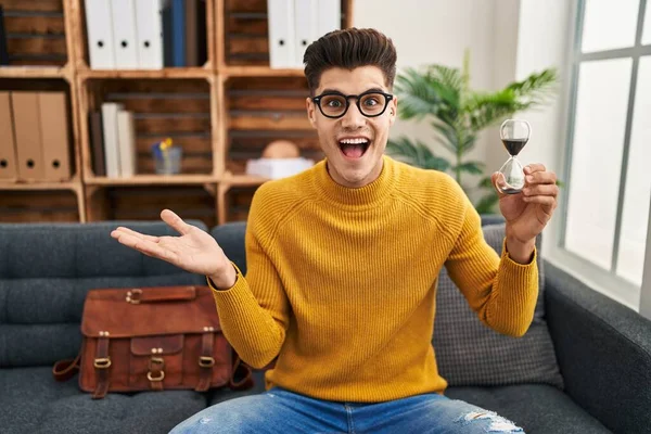 Young Hispanic Man Holding Sand Clock Celebrating Achievement Happy Smile — 스톡 사진