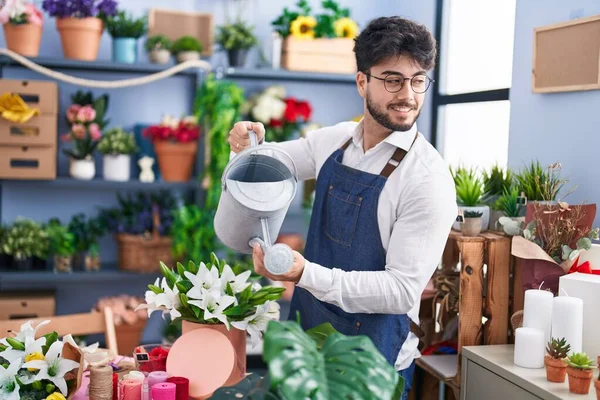 Young hispanic man florist smiling confident watering flowers at florist shop