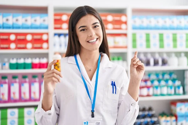 在药店工作的西班牙裔妇女微笑着拿着药丸 高兴地手指手画脚 — 图库照片