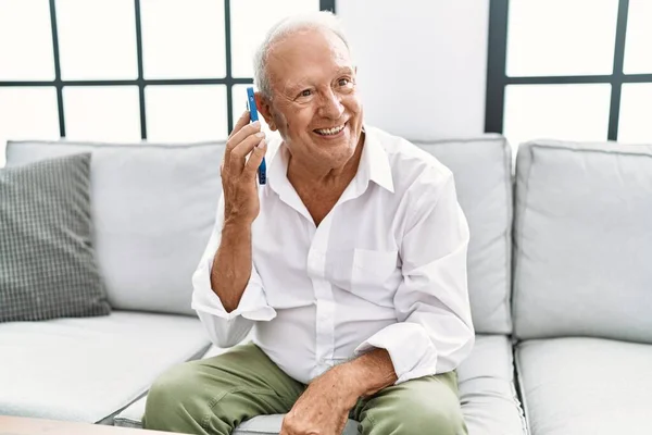 Senior man smiling confident using smartphone at home