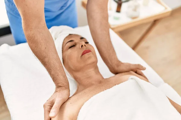 Middle age man and woman wearing therapist uniform having shoulders massage session at beauty center