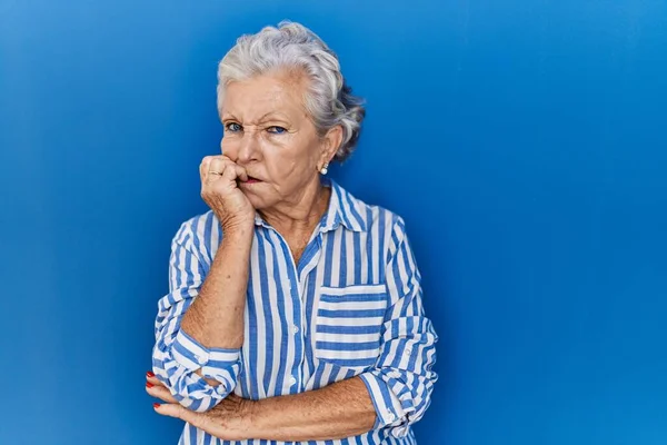 头发灰白的老妇人站在蓝色的背景上 满脸紧张 双手放在咬指甲的嘴上 焦虑问题 — 图库照片