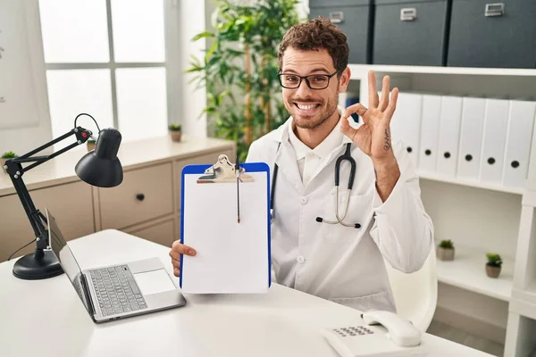 Young Hispanic Man Wearing Doctor Stethoscope Holding Clipboard Doing Sign — Stock Photo, Image