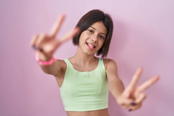 小女孩站在粉红的背景上笑着 伸出双手的手指做胜利的手势 第二点 — 图库照片