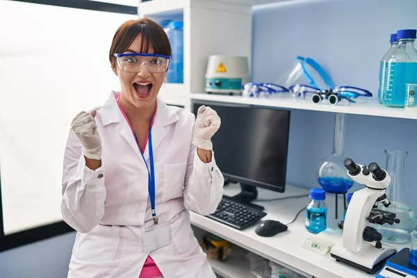 科学研究所で働いている若いブルネットの女性は驚きを祝い 腕を上げて目を開けて成功したことに驚いています 勝者のコンセプト — ストック写真