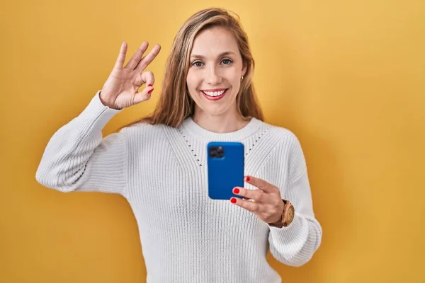 スマートフォンの入力メッセージを使用して若いブロンドの女性は 手と指でOkサインを行う肯定的な笑顔 成功した表現 — ストック写真