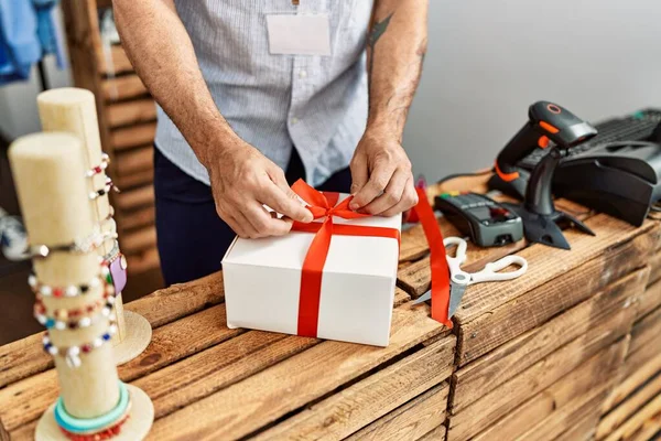 Hands of shopkeeper man preparing gift at clothing store.