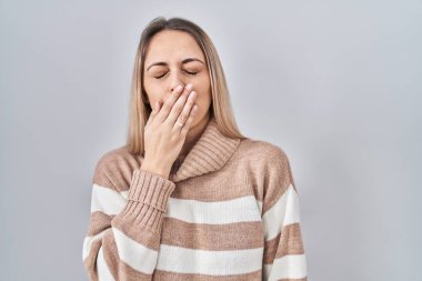 İzole edilmiş arka planda balıkçı yaka kazak giyen genç sarışın kadın ağzıyla esnemekten sıkılmış. Huzursuz ve uykulu.. 