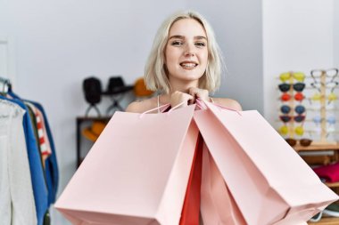 Giysi dükkanında kendine güvenen, gülümseyen beyaz bir kadın.