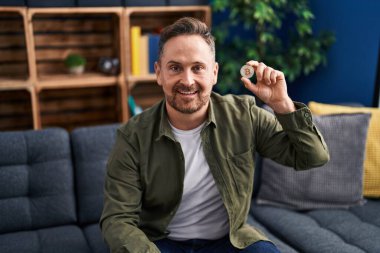 Orta yaşlı, elinde sanal para olan beyaz bir adam pozitif ve mutlu görünüyor ve kendine güvenen bir gülümsemeyle dişlerini gösteriyor. 