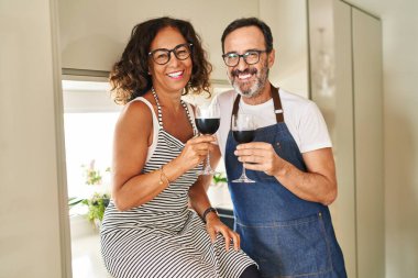 Orta yaşlı İspanyol çift, mutfakta şarapla kadeh kaldırırken gülümsüyor.