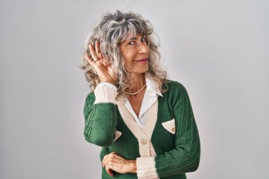 Beyaz arka planda dikilen orta yaşlı bir kadın kulağına fısıldayarak dedikoduları ve dedikoduları dinliyor. Sağırlık kavramı. 