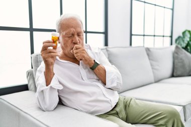 Senior man holding pills feeling unwell and coughing as symptom for cold or bronchitis. health care concept. 