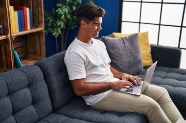 Evdeki masada dizüstü bilgisayar kullanan genç bir İspanyol.
