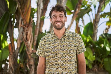 Genç İspanyol adam parkta yürürken kendinden emin gülümsüyor.