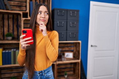 Genç esmer kadın akıllı telefon kullanıyor. Ciddi yüz ifadesi var. Soruları sorarken çenesi üstüne el ele düşünüyor. 