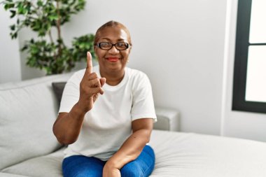Olgun İspanyol kadın evdeki kanepede oturuyor ve bir numaralı parmağı gösterip işaret ederken kendinden emin ve mutlu gülümsüyor.. 