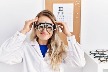 Young beautiful optician woman wearing optometry glasses at the clinic suffering from headache desperate and stressed because pain and migraine. hands on head. 