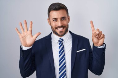 Yakışıklı İspanyol takım elbiseli ve kravatlı adam altı numaralı parmaklarını gösterip gösterirken kendinden emin ve mutlu gülümsüyor.. 