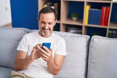 Middle age man using smartphone sitting on sofa at home