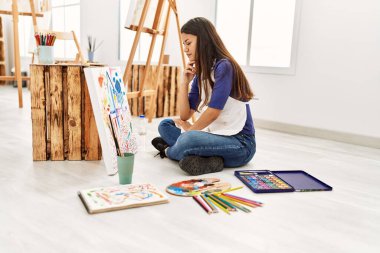 Resim stüdyosunda resim çizen şüpheyle bakan genç Latin kadın.