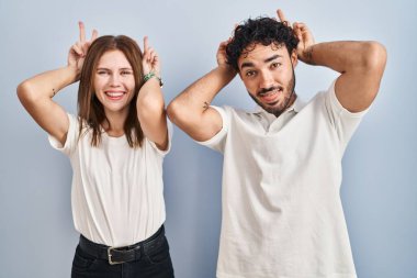 Genç bir çift, günlük giysiler giyip birbirlerine komik ve çılgın pozlar veriyorlar. Parmakları kafalarında tavşan kulakları, neşeli bir gülümseme. 