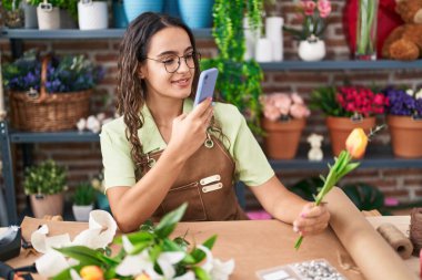 Genç ve güzel İspanyol çiçekçi çiçekçi çiçekçide çiçekçide akıllı telefonla fotoğraf çekiyor.