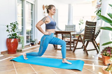 Güzel bir beyaz kadın evindeki terasta antrenman yapıyor ve esniyor. Asya 'da ve sağlıkta yoga minderinde çalışıyorum..