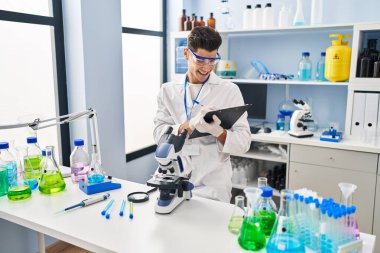 Laboratuvarda panoya yazı yazan, bilim adamı üniforması giyen İspanyol bir genç.