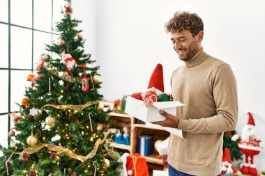 Genç İspanyol adam gülümsüyor. Evde kendine güvenen bir Noel ağacı süslüyordu.