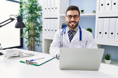 Klinikte çalışan dizüstü bilgisayar kullanan doktor üniforması giyen genç bir İspanyol.