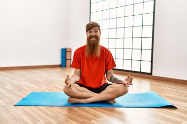 Genç kızıl saçlı, gülümseyen, spor merkezinde yoga eğitimi alan kendine güvenen bir adam.