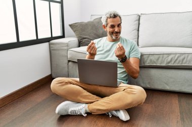 Orta yaşlı İspanyol bir adam oturma odasında dizüstü bilgisayar kullanıyor. Elleriyle para hareketi yapıyor. Maaş istiyor. 