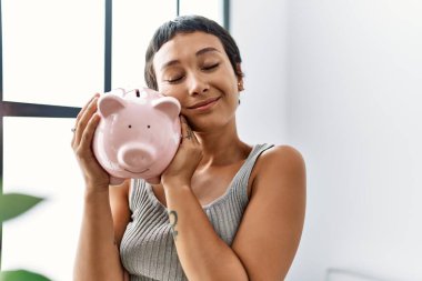 Genç İspanyol kadın gülümsüyor. Kumbarasını evinde tutuyor.