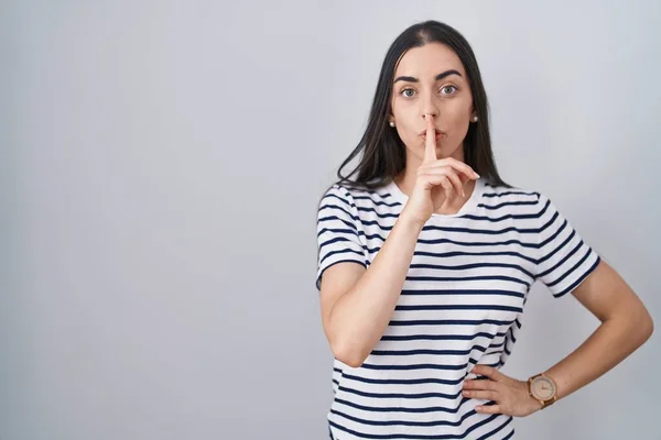 若いブルネットの女性は唇に指で静かになるように求める縞模様のTシャツを着ていた 沈黙と秘密の概念 — ストック写真
