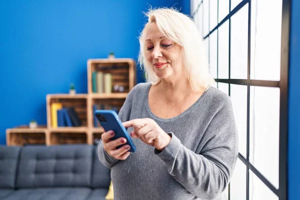 Middle Age Blonde Woman Using Smartphone Standing Home — Stockfoto